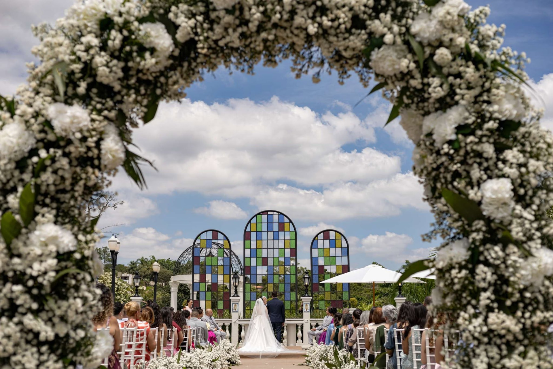 Cerimônia de casamento ao ar livre com arco de flores brancas sob o céu azul